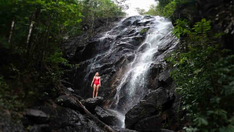 Woman in a red swimsuit standing in front of a waterfall in Koh Phangan Thailand