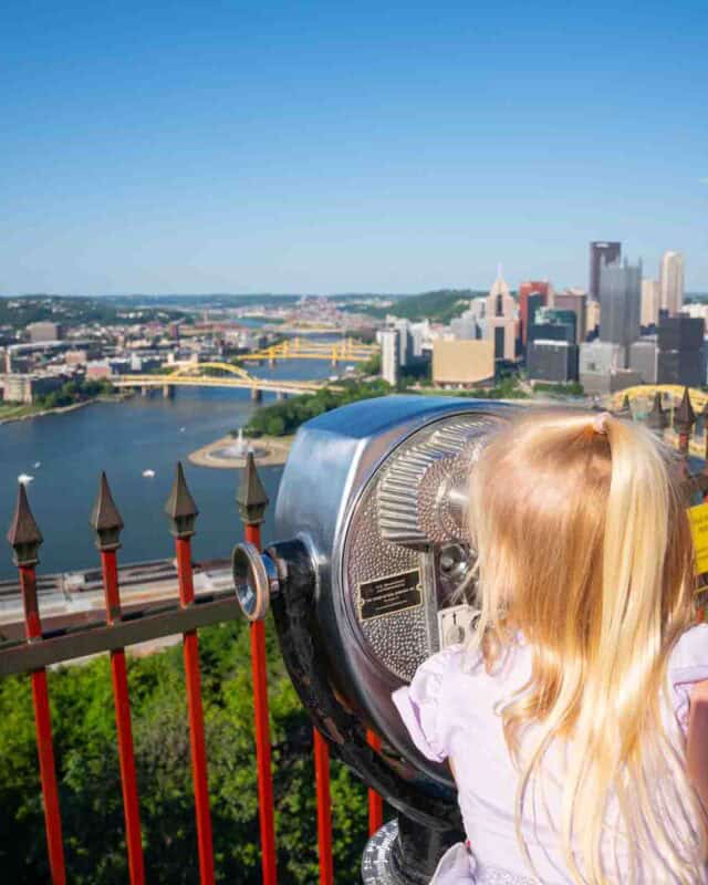 little girl looking though buniculars at the the Duquesne Incline looking at Pittsburgh skyline